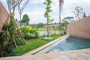 A swimming pool with a stone border, surrounded by lush greenery and a view of a water body.