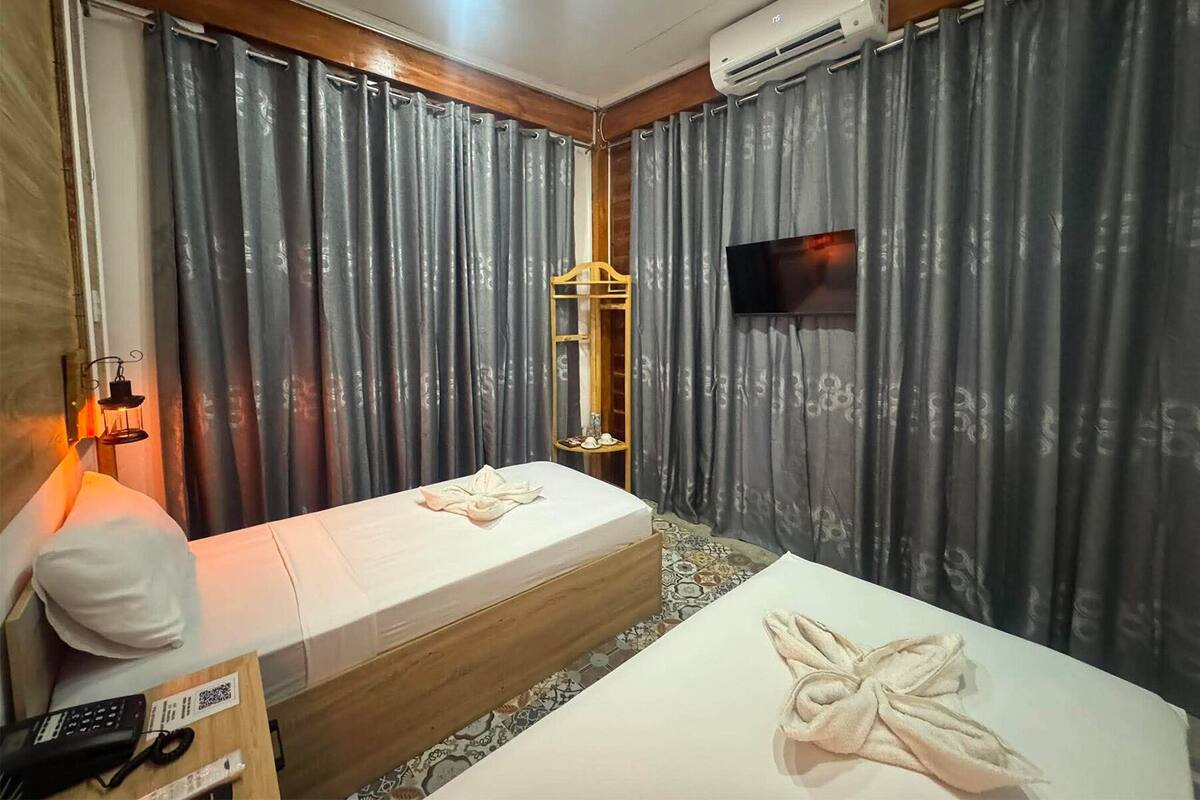 A hotel room with two beds, a TV, an air conditioner, and a small table with a remote control.