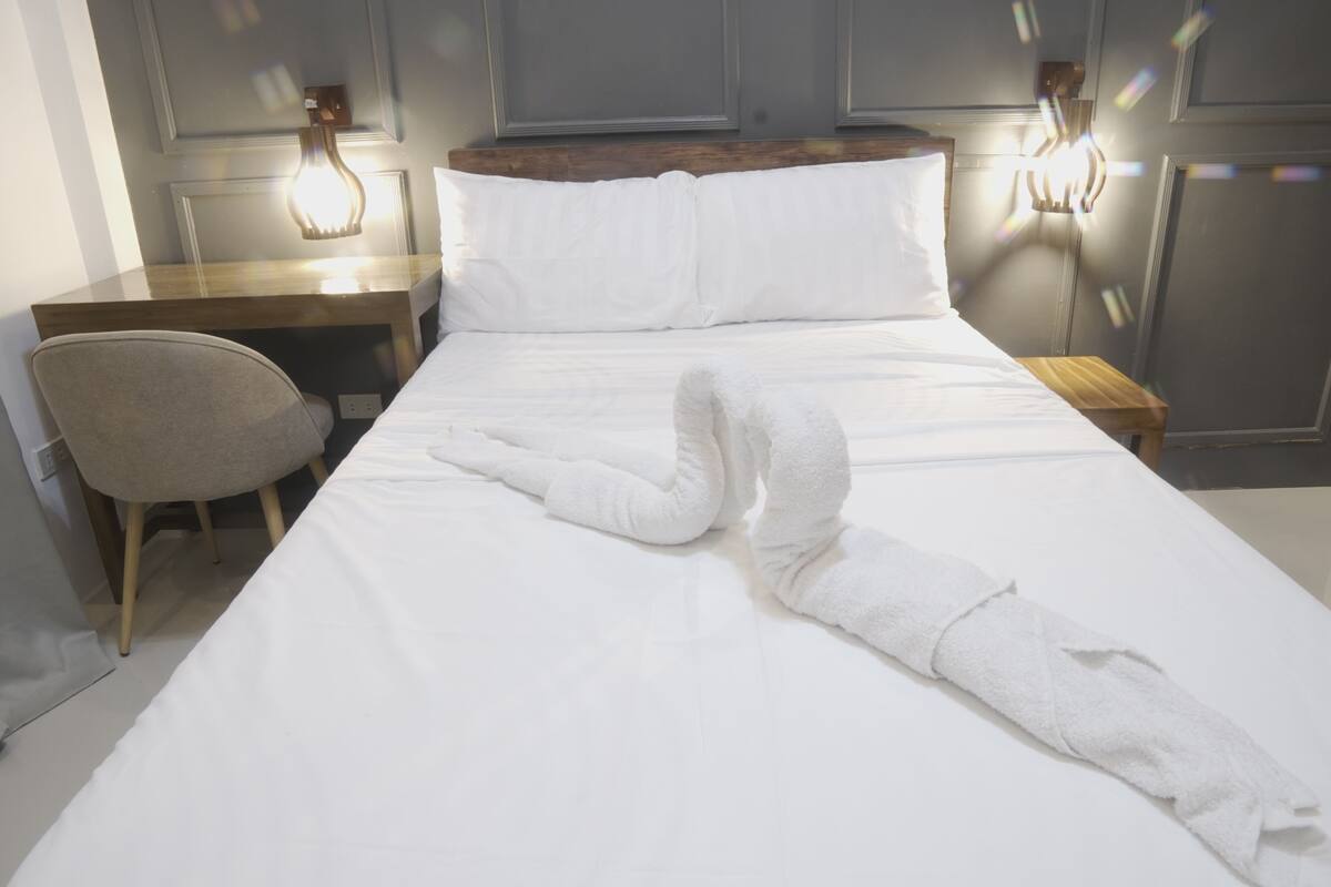 A neatly made bed with a towel, a chair, and a nightstand with a lamp.