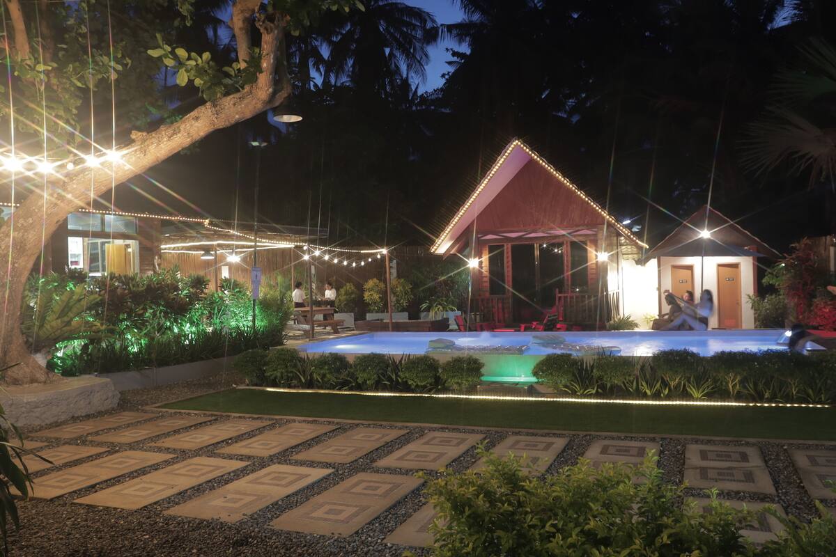 A well-lit outdoor area with a pool, seating, and a building with a red roof.