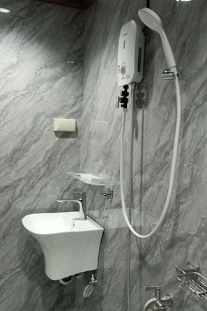 A bathroom with a marble wall, a white sink, a handheld showerhead, and a handheld shower attachment. - Rue DeuxVilles Villa (Loon)