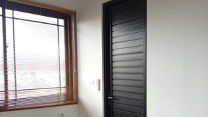 Ein Schlafzimmer mit Bett, Fenster mit Jalousien und einer Tür.