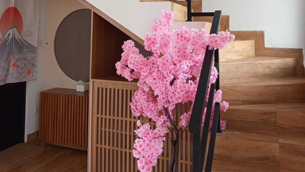Eine Treppe mit hölzernen Stufen und schwarzen Geländern, ein Topf mit Kirschblüten und eine Wand mit japanischem Dekor.