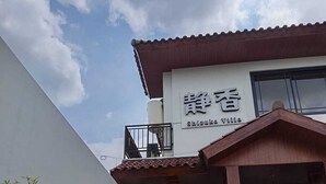 Ein Gebäude mit einem Schild, auf dem 'Shizuka Villa' steht, und einem überdachten Eingangsbereich mit einer kleinen Gartenanlage.