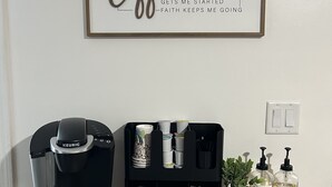 Una cafetera, un soporte para cápsulas de café y dos botellas de jabón líquido sobre una superficie de madera.