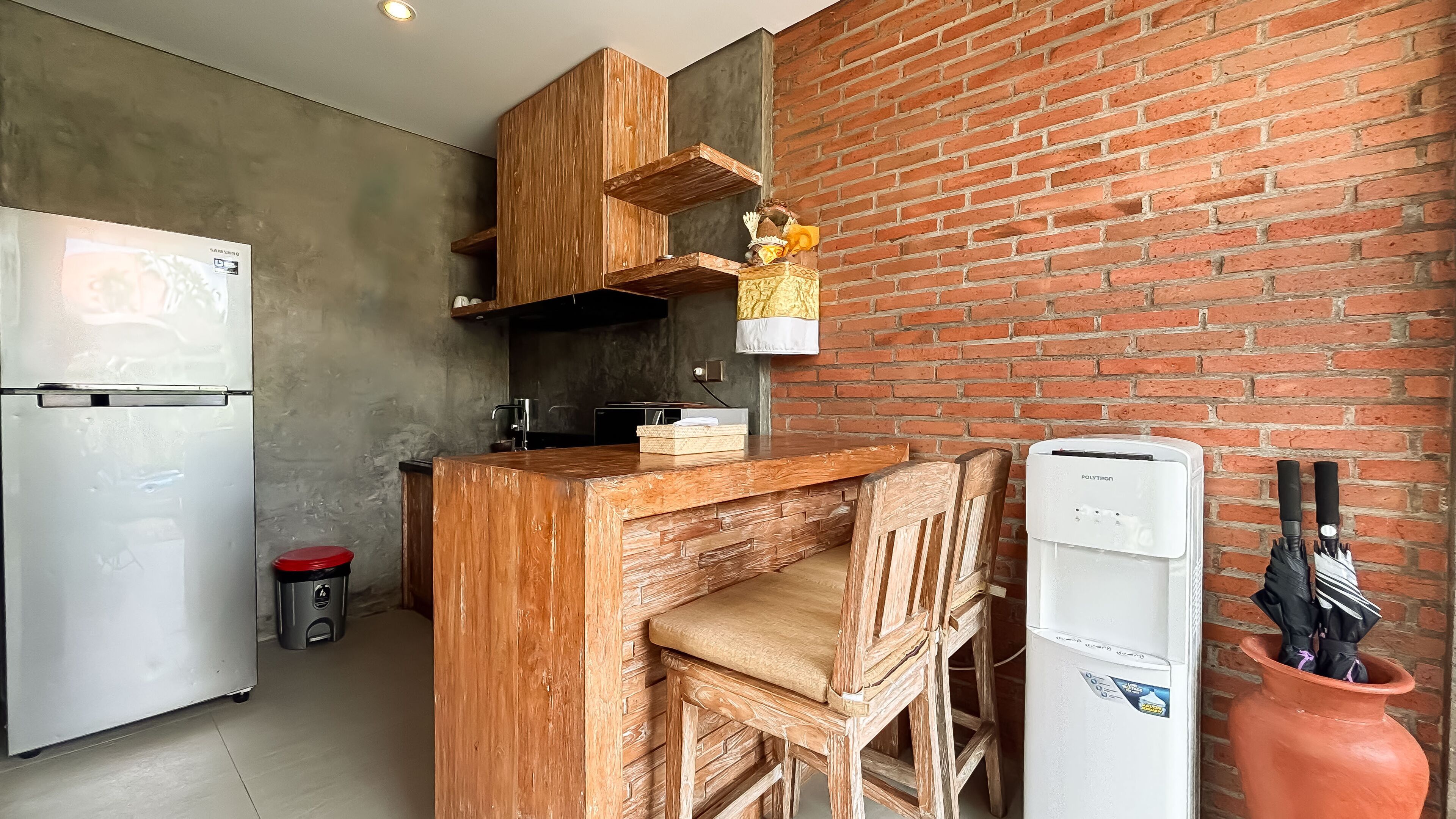 A kitchen with a refrigerator, wooden cabinets, a brick wall, and a white appliance.