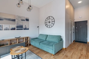 A modern living room with a teal sofa, a wooden coffee table, a wall clock, and a series of framed pictures.