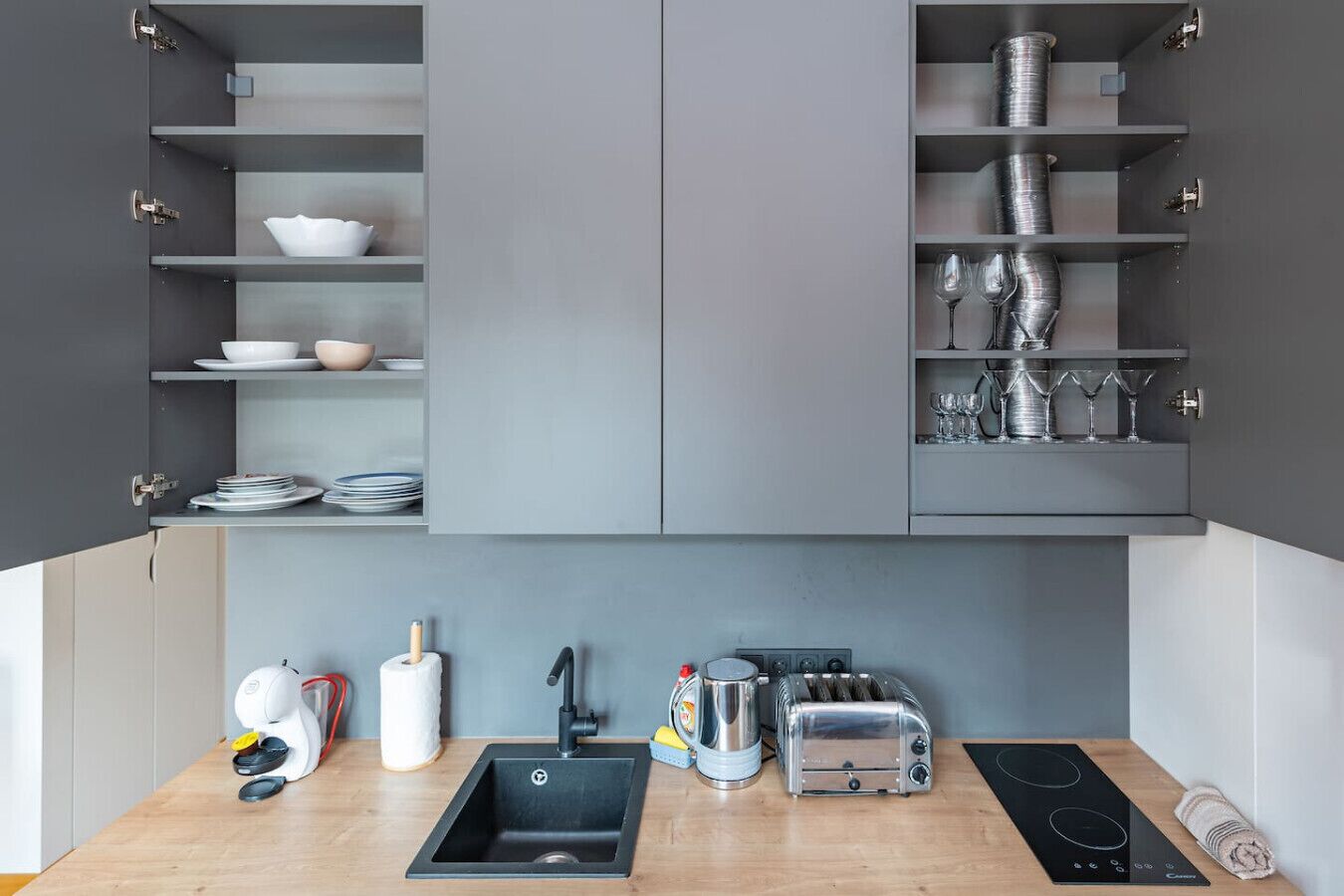 Une cuisine moderne avec des meubles gris, un évier noir, un grille-pain, une bouilloire et un four encastré.
