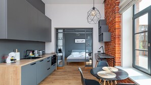 Cocina compacta con electrodomésticos modernos, comedor con mesa y sillas, cama con vistas, y pared de ladrillo.