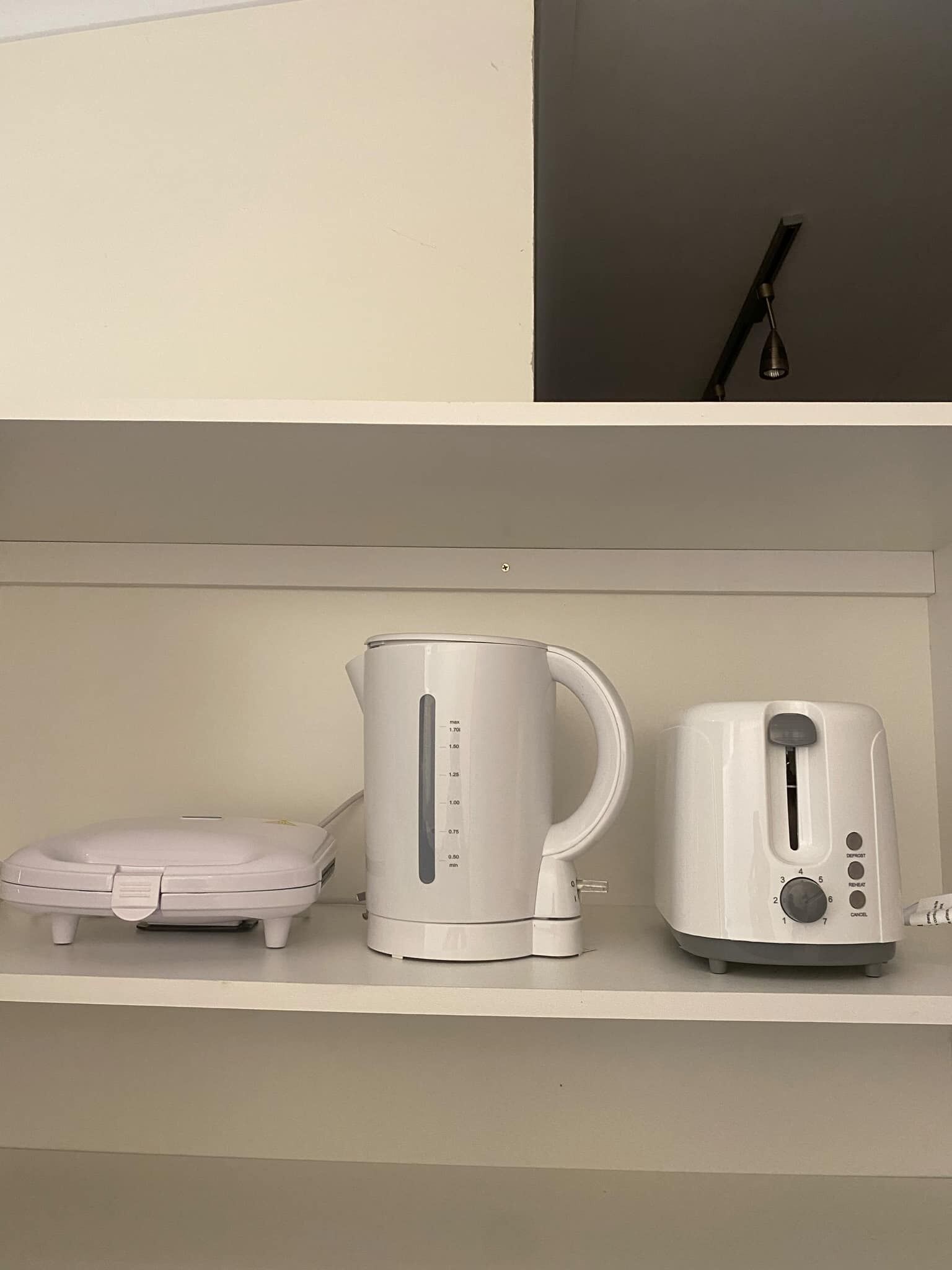 A kitchen with a white kettle, a toaster, and a small appliance on a white shelf.