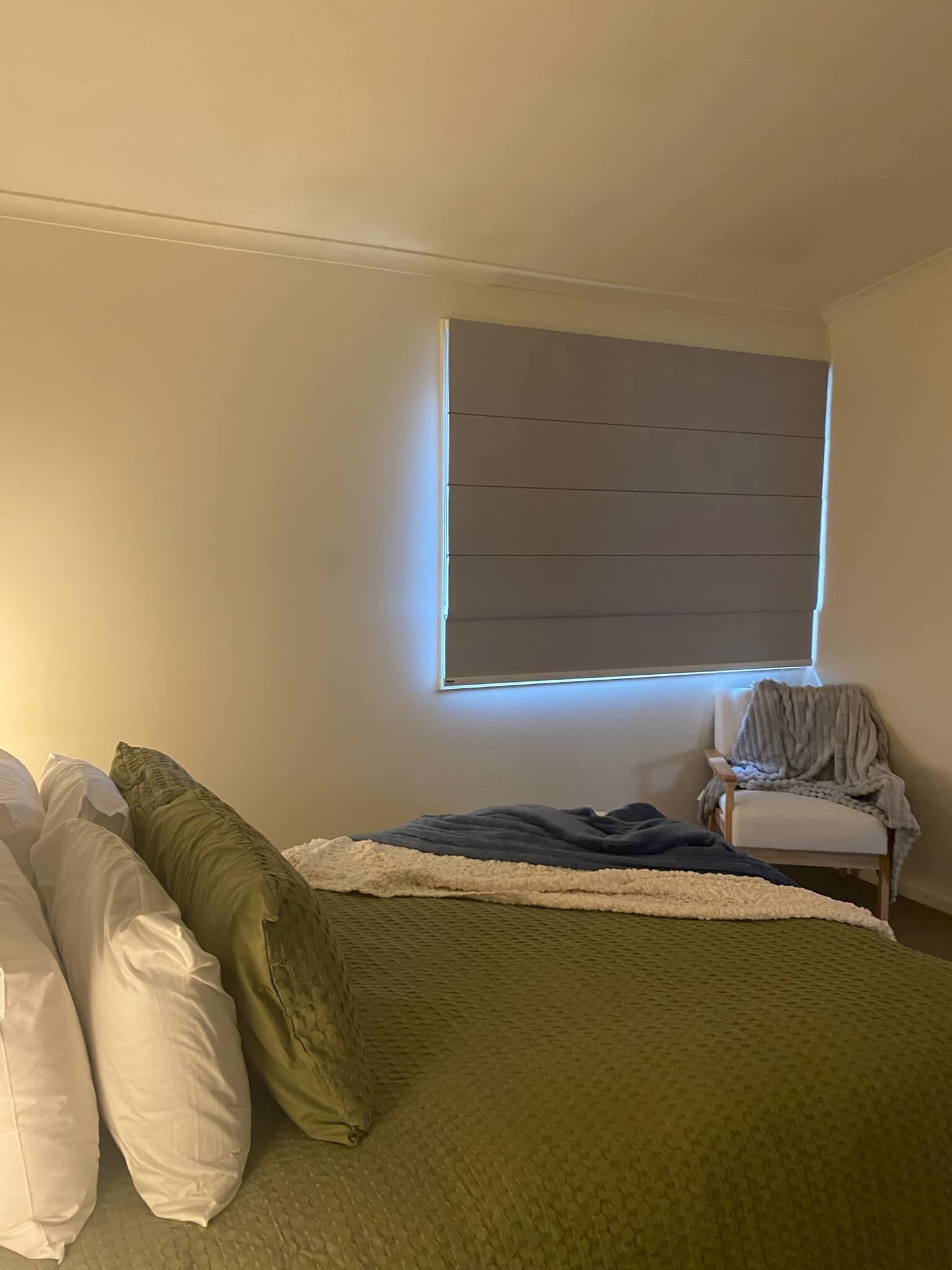 A bedroom with a bed, pillows, a chair, and a window with blinds.