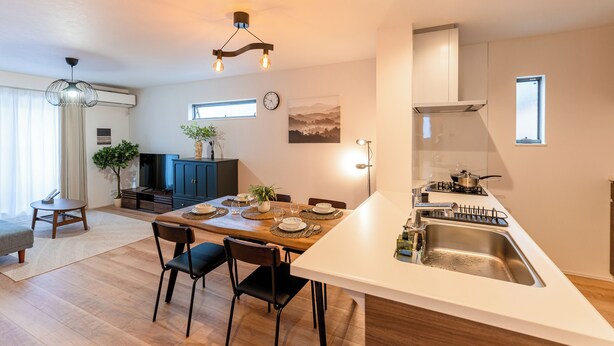 A modern kitchen with a central island, a dining area with a wooden table and chairs, and a living area with a sofa and a coffee table.