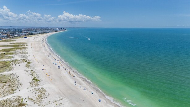 Une plage côtière avec une longue étendue de sable, une mer bleue et limpide, et une vue lointaine sur les gratte-ciel d’une ville.