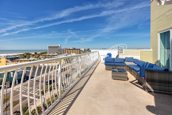 A rooftop terrace with a view of the beach and cityscape, furnished with wicker sofas and a small table.