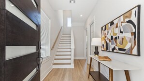 A modern hallway with a staircase, a white console table with a lamp, and a large abstract painting on the wall.