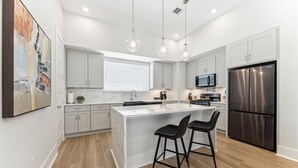 A modern kitchen with white cabinets, a stainless steel refrigerator, and pendant lighting.
