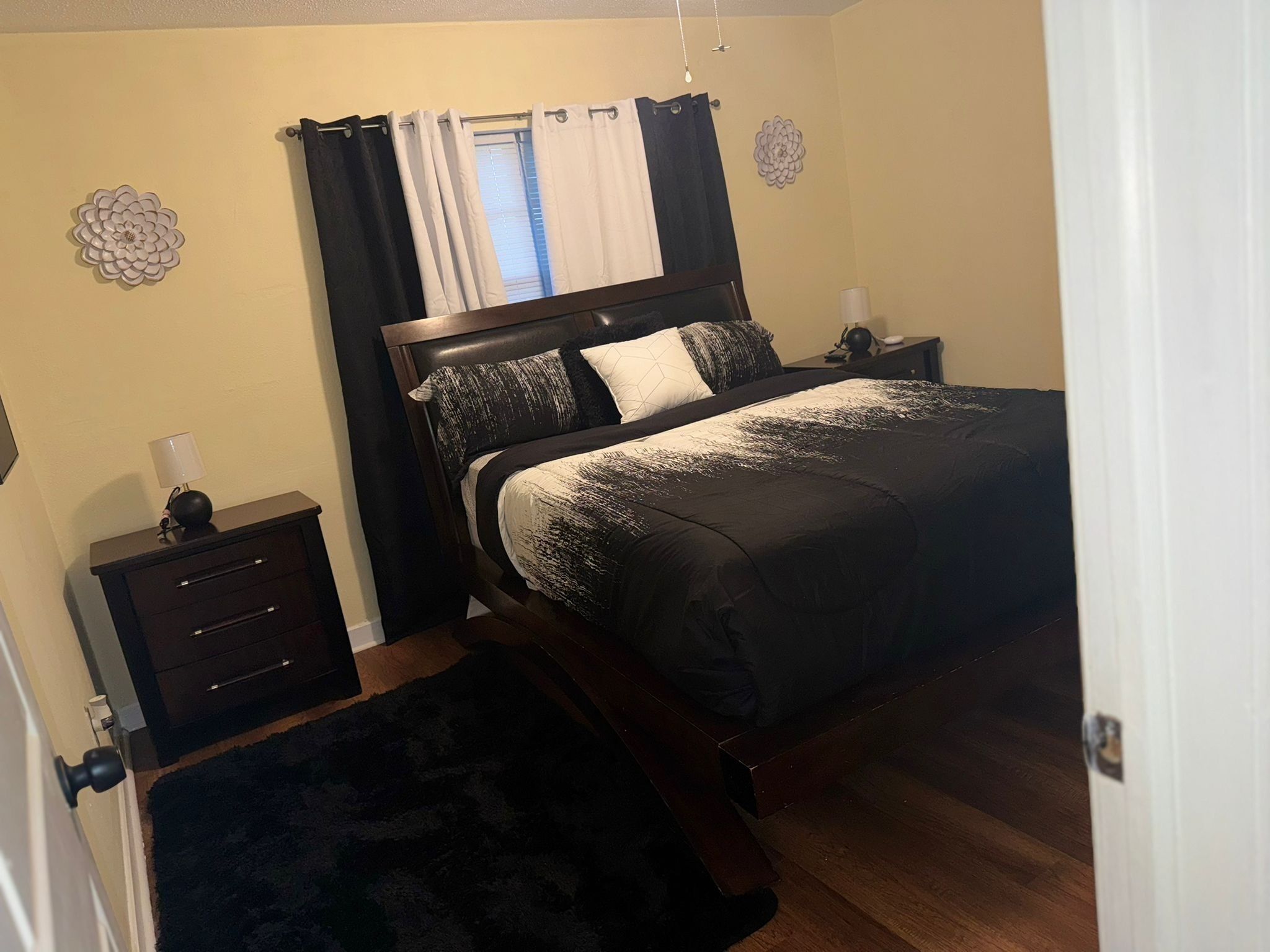 A bedroom with a bed, a nightstand, a lamp, and a dark rug.