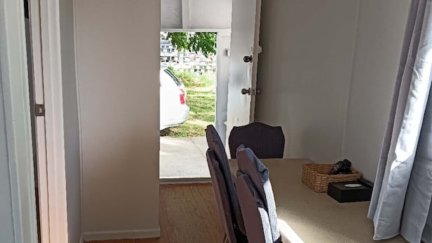 Una habitación pequeña con suelo de madera, una mesita, un banco y una puerta que da al exterior.