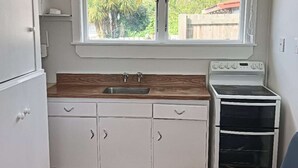 Una cocina compacta con armarios blancos, una encimera de madera, un fregadero y una estufa.