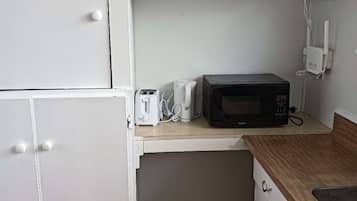 A compact kitchen with white cabinets, a microwave, a toaster, and a small trash bin.