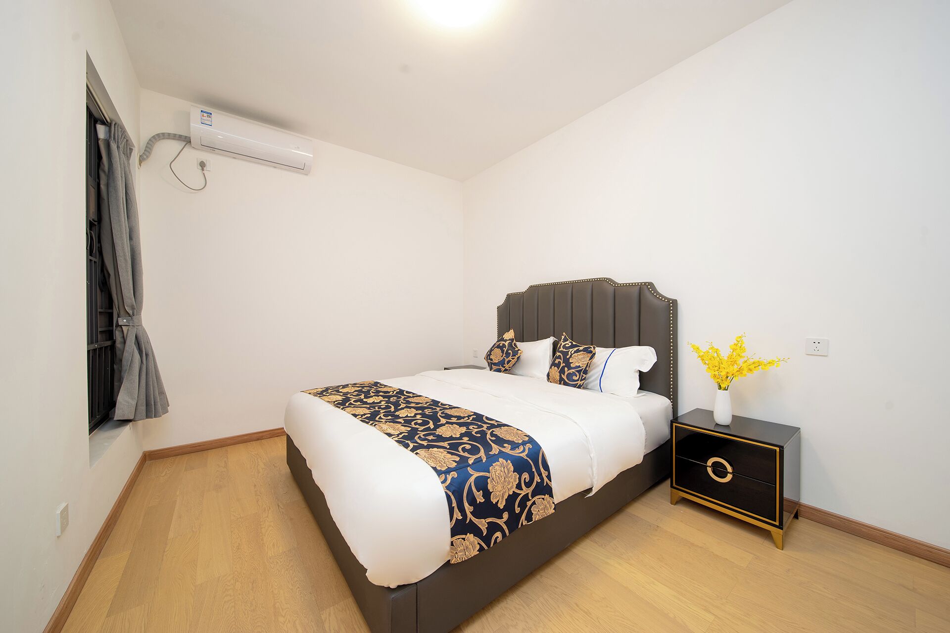 A bedroom with a bed, bedside table, and a wall-mounted air conditioner.