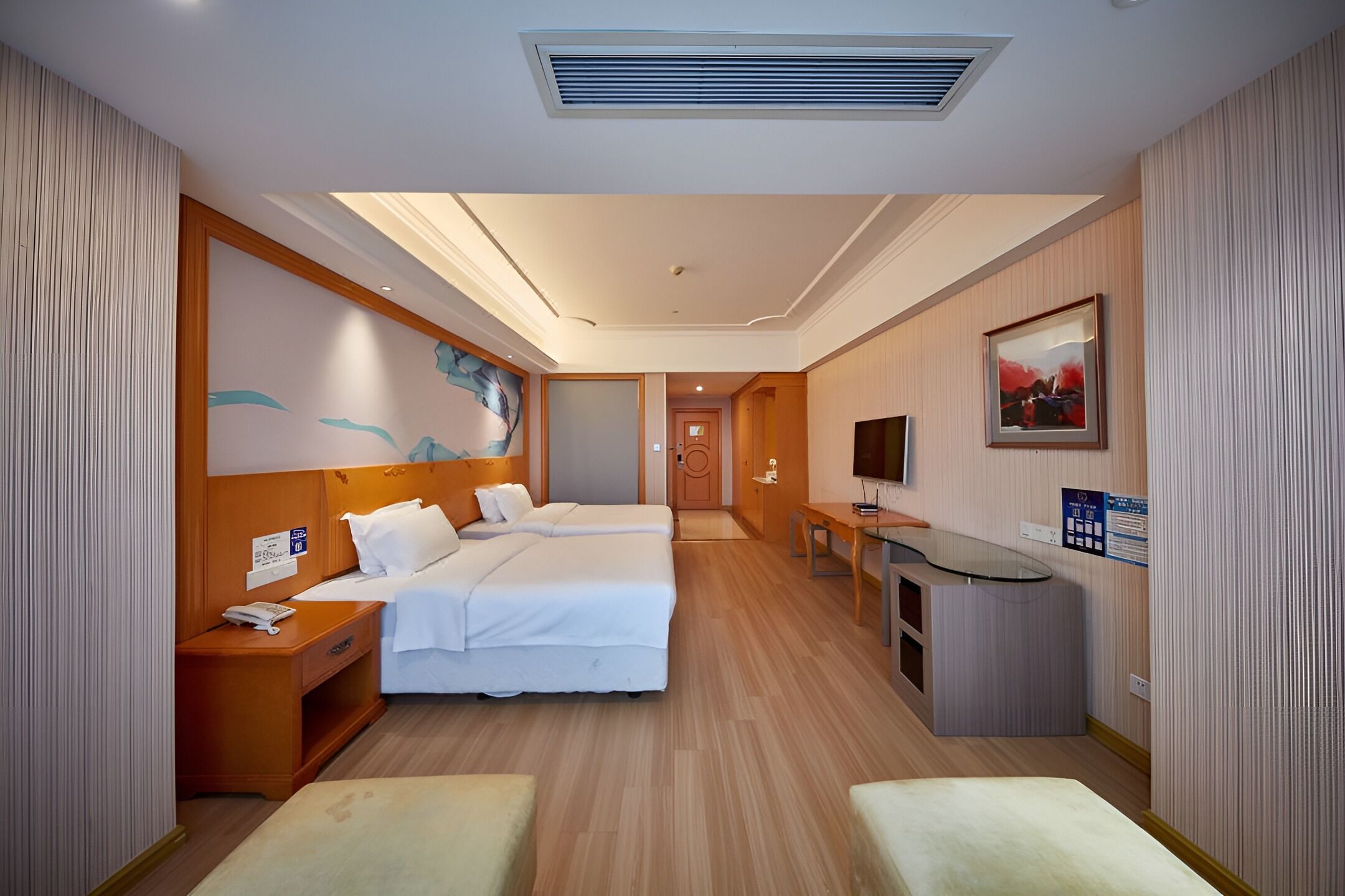 A hotel room with two beds, a desk, a TV, and a small kitchenette.