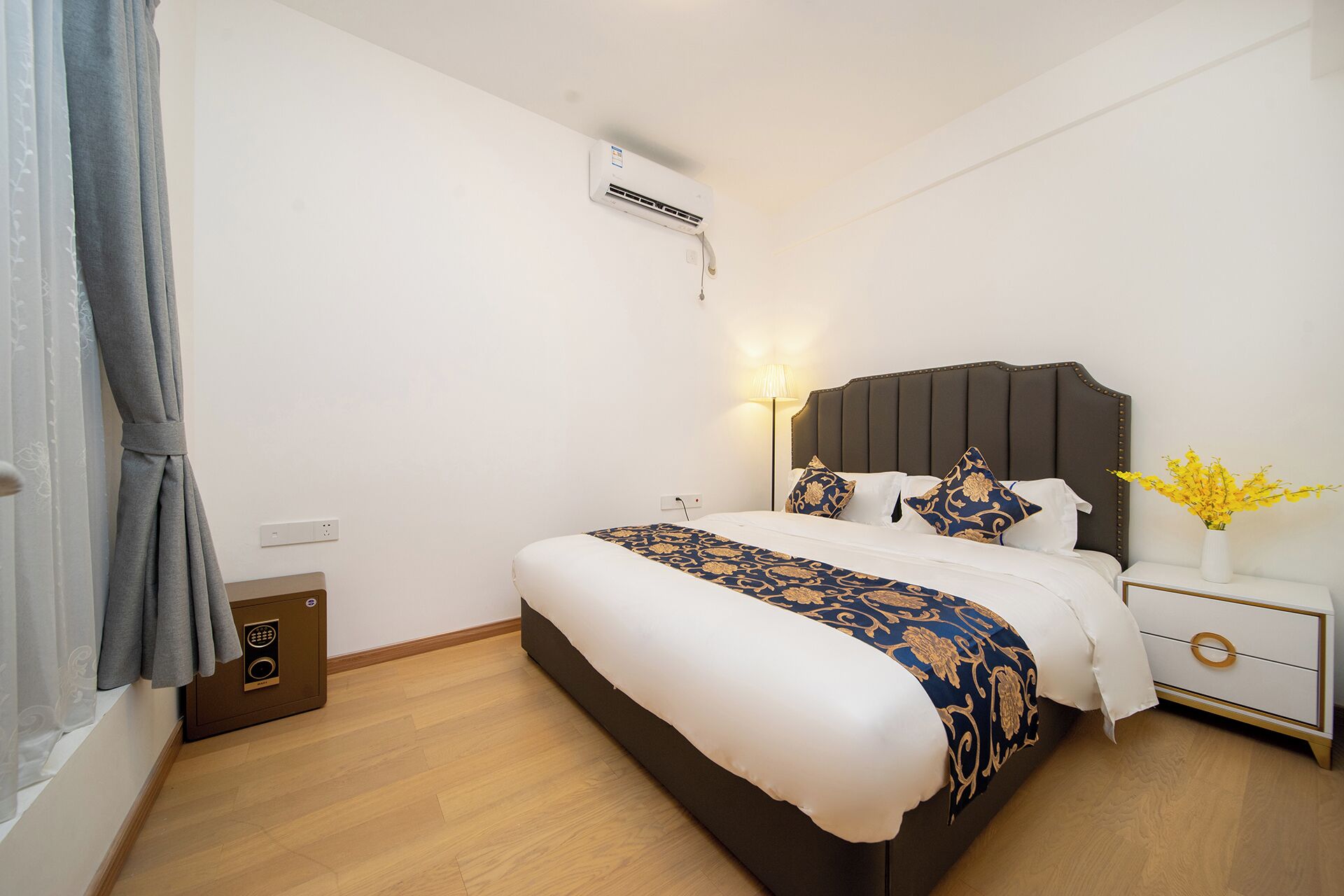 Habitació d'hotel amb llit, taula de nit, làmpada i aire condicionat.