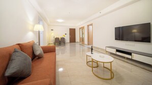 Een moderne woonkamer met een bank, een televisie en een eethoek op de achtergrond.