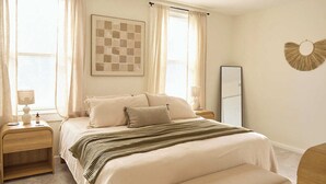 Een slaapkamer met een bed, nachtkastjes, een plafondventilator, een grote spiegel en een decoratief object aan de muur.