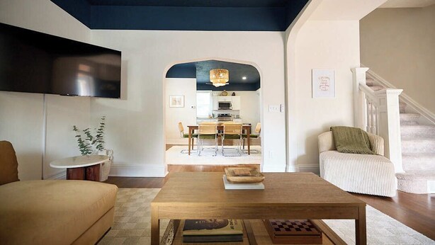 Een woonkamer met een houten salontafel, een bank en een aan de muur bevestigde televisie. Er is een trap die naar een ander niveau leidt.
