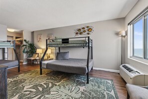 Une chambre avec un lit superposé, un bureau, une chaise, une lampe et une grande fenêtre.