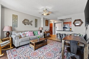 A living room with a sofa, coffee table, and chairs, a dining area with a table and chairs, and a kitchen with appliances.