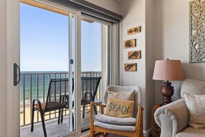 A room with a view of the ocean, a chair with a 'BEACH' pillow, and a lamp.