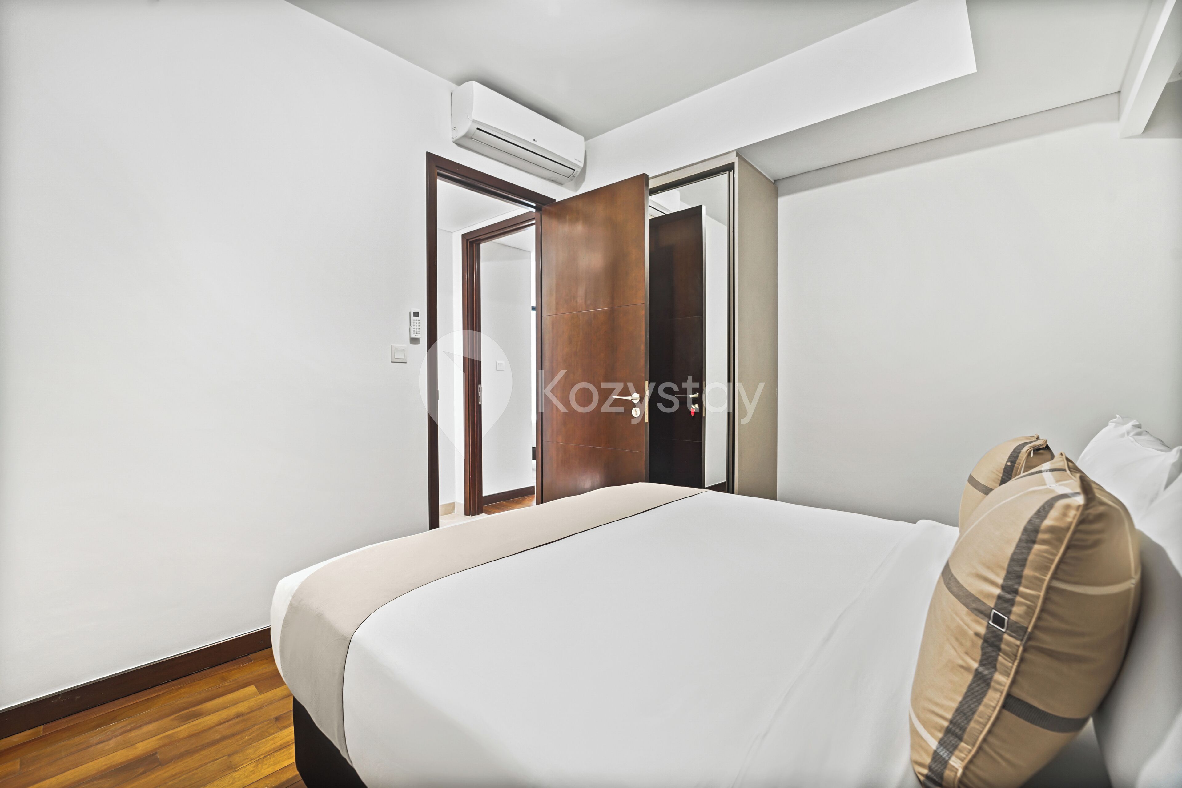 A modern bedroom with a large bed, wooden flooring, white walls, and an air conditioning unit.