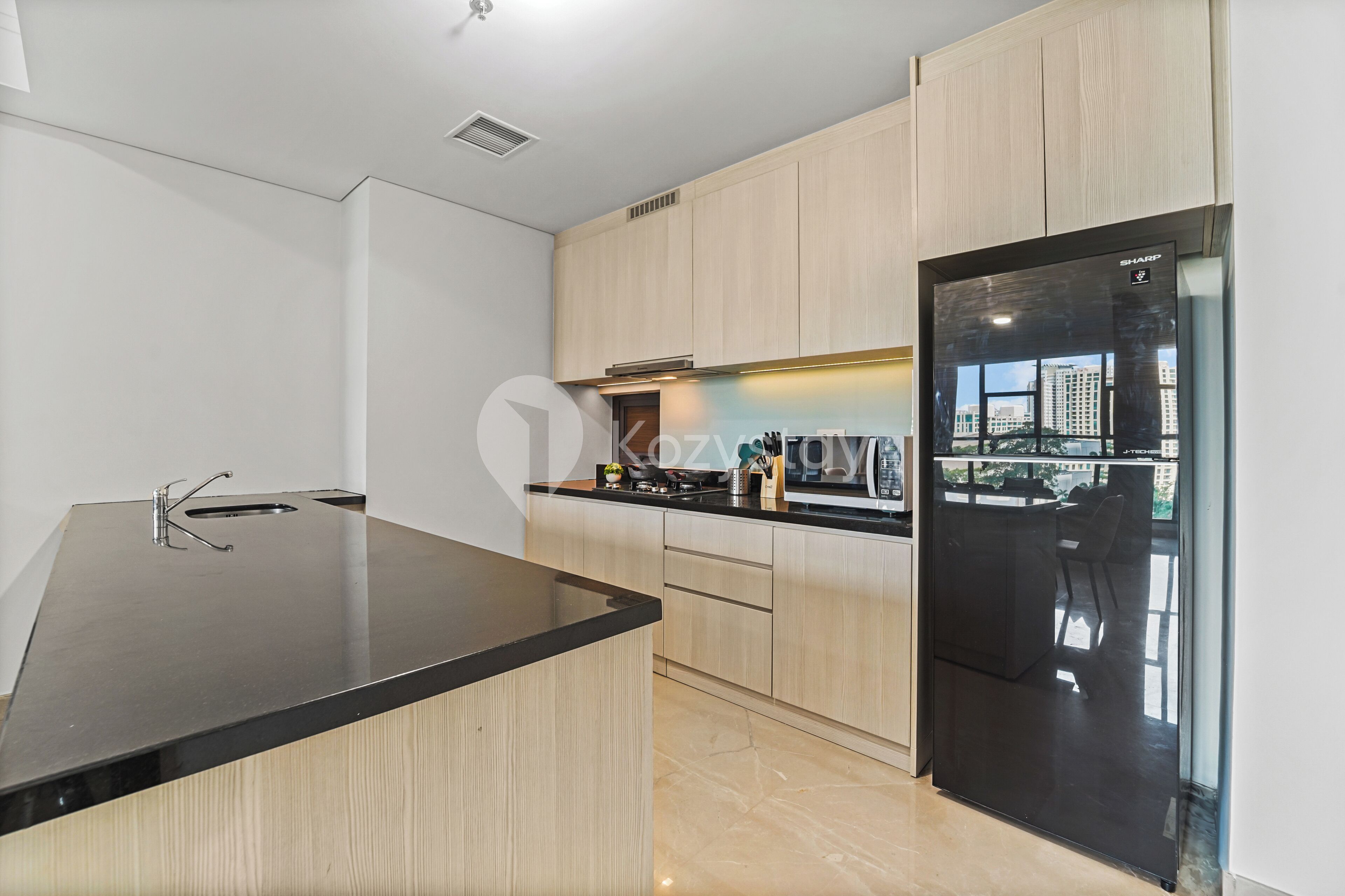 A modern kitchen with a black countertop, wooden cabinets, and a large refrigerator with a city view.