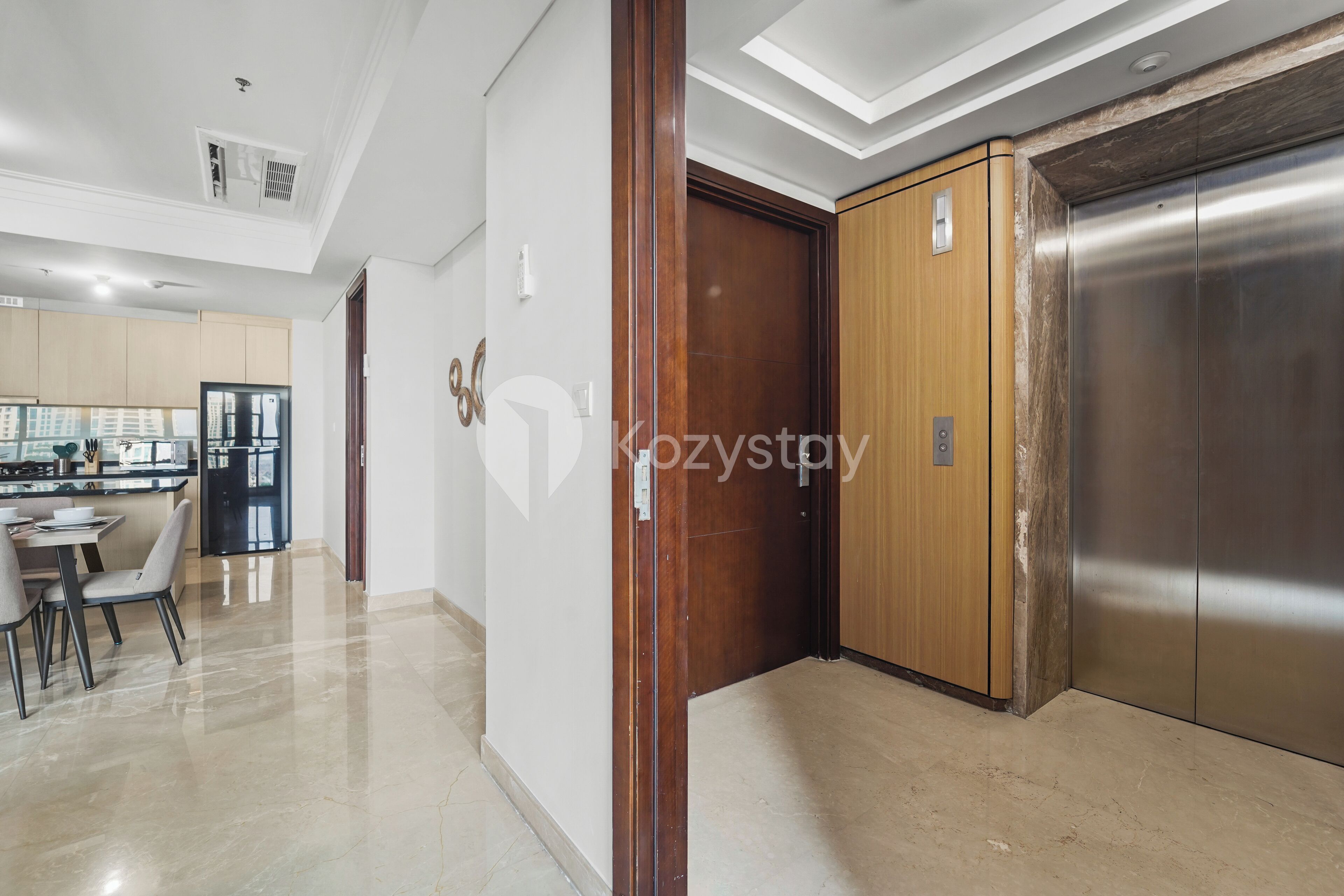 A modern kitchen with a dining area, a wooden door, and a stainless steel elevator.