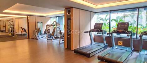 A modern gym with treadmills, weight machines, and a large window with a view of greenery.