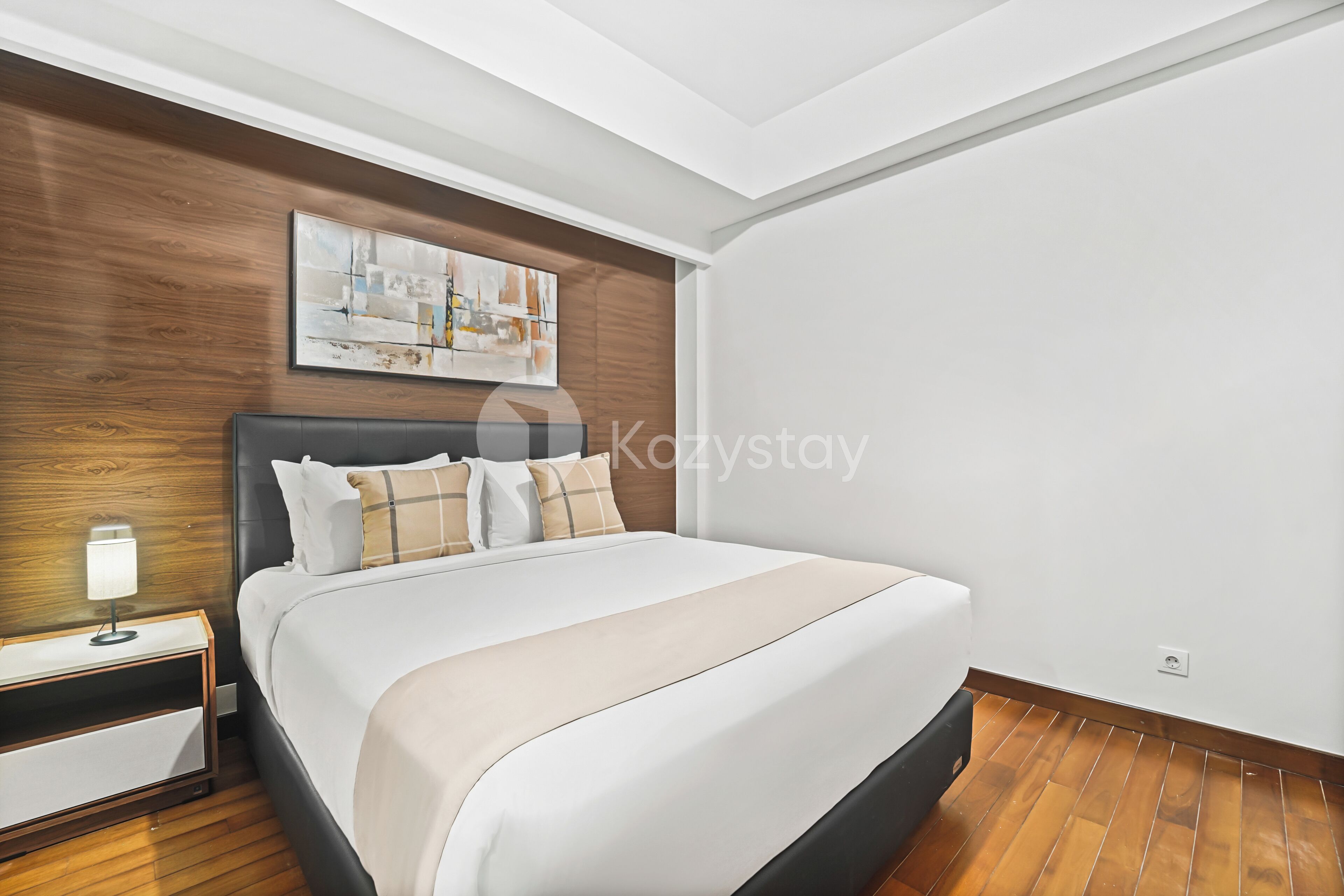 A modern hotel room with a large bed, wooden panel wall, and a painting above the bed.