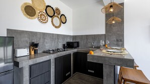 A modern kitchen with a central island, dark cabinetry, and a backsplash with woven wall art. - Oceanview Escape 1BR Villa Bingin, Uluwatu (Bali)