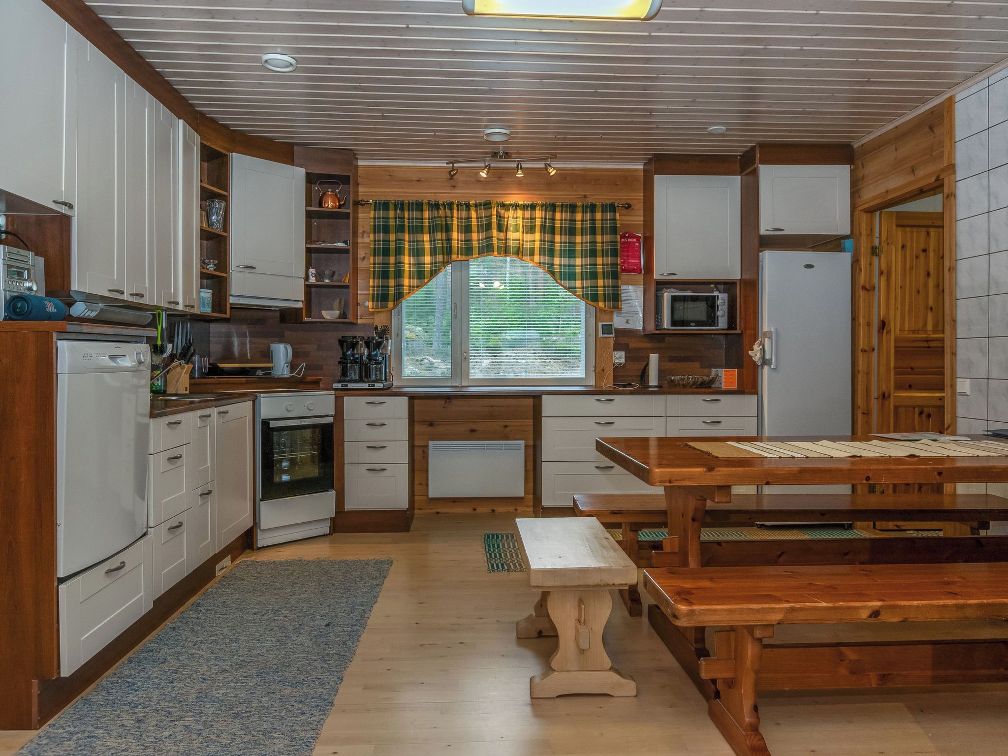 Een kleine keuken met witte kasten, een inbouwoven, een magnetron en een houten eettafel.