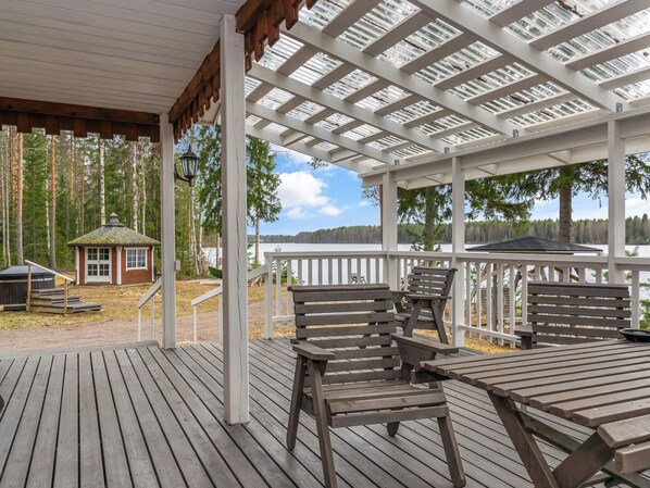 A wooden deck with benches and tables, overlooking a lake with a small cabin in the background.