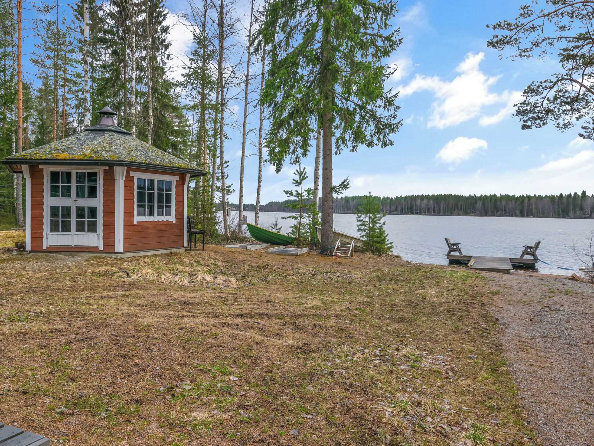 En stuga med en liten veranda och en brygga som sträcker sig ut i en sjö, omgiven av träd.