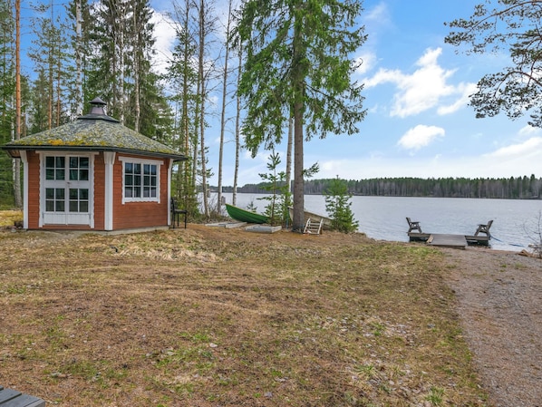 A cabin with a small deck and a dock extending into a lake, surrounded by trees.