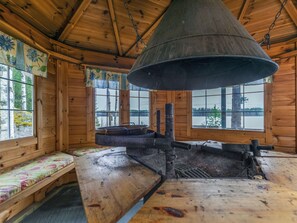 A rustic cabin interior with a large metal stove, wooden benches, and large windows offering views of a forested landscape. - Louhuranta by Interhome (Karstula)