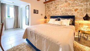 Ein Schlafzimmer mit Steinsturz, einem Bett mit blauer Kopfteil und einer Holzbalkendecke.