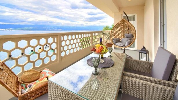 Ein Balkon mit Korbmöbeln, einem Hängesessel und einem Tisch mit Obstschale und Glas.
