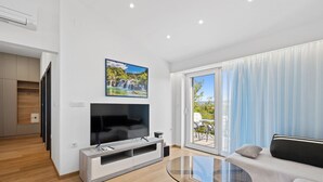 A modern living room with a flat-screen TV, a glass coffee table, a sofa, and a sliding glass door leading to a balcony. - Holiday Home Eros (Sibenik)