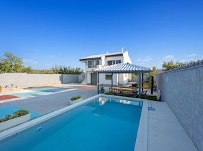 Ein modernes Haus mit Swimmingpool, einer überdachten Terrasse und Blick auf die Umgebung.