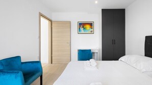 A modern hotel room with a bed, a blue chair, a desk, and a wardrobe. - Holiday Home Eros (Sibenik)