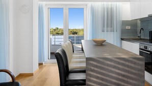 A modern kitchen with a large island, a dining area with a long table and chairs, and a view of greenery through the windows. - Holiday Home Eros (Sibenik)